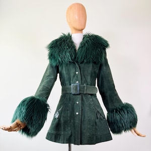 May include: A dark green suede coat with a faux fur collar and cuffs. The coat features a belted waist, button closures, and pockets. The mannequin is wearing the coat. The coat is a vintage style.