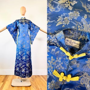 May include: A vintage blue dress with a floral pattern and yellow frog closures. The dress has wide sleeves and a mandarin collar. The label reads "Royal Hawaiian Quality Garment Made in Honolulu".