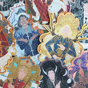 Puede incluir: Una colección de pegatinas ilustradas y coloridas con varios personajes. Las pegatinas muestran ilustraciones detalladas con detalles dorados y brillantes. Los diseños incluyen figuras con ropa ornamentada, con elementos de texto y bordes decorativos.