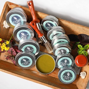 May include: A collection of 10 round tins with blue and white labels featuring an owl design. The labels read "Wise Owl Furniture Salve" and list different scents like "Noir Moon", "Black Sea", "White Tea", and "Lemon Verbena".