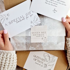 May include: A brown cardboard box with a white tissue paper lining. The box contains a white card with the text "A SPECIAL GIFT handmade for you" and a white card with the text "QUEEN BEE GIFTBOX handmade for you".