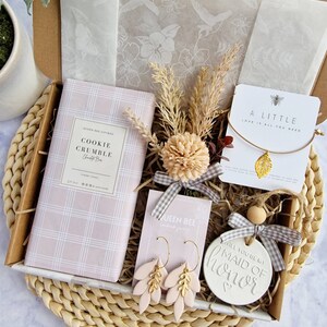 May include: A gift box filled with items for a maid of honor. The box includes a cookie crumble bar, a pair of gold and pink earrings, a small wooden sign that says "Will you be my Maid of Honor", and a small card that says "A Little Love is All You Need".