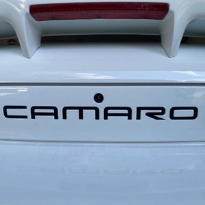 May include: A white ceramic mug with a black handle and the text "But First, Coffee" in a black, bold font. The mug is sitting on a wooden surface. The mug is 4 inches tall.