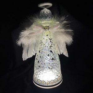 May include: A white angel figurine made from a glass bottle with a halo, white feathers, and a white and pink ribbon. The bottle is covered in iridescent glitter and has a white light inside.