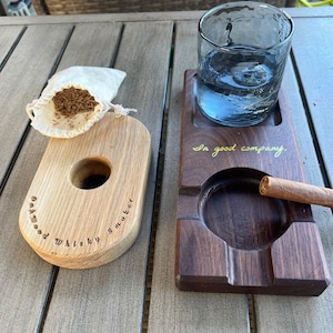 May include: Two wooden trays, one with a small bag of tobacco and the text "Oakwood Whisky Smuggler" and the other with a glass of water and the text "In good company".