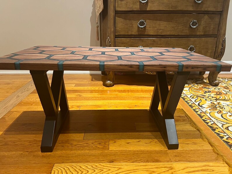 May include: A rectangular coffee table with a wooden top featuring a honeycomb design with teal resin inlays. The table is supported by black metal legs, creating a modern aesthetic. The table measures approximately 48 inches long and 24 inches wide.