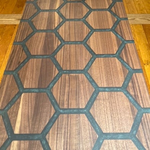 May include: A rectangular wooden table with a honeycomb design. The table's surface features a natural wood grain pattern, with dark gray epoxy resin filling the hexagonal cells. The table is a medium brown color.