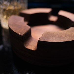 May include: A dark brown wooden ashtray with four compartments. The ashtray is round and has a smooth, polished finish.