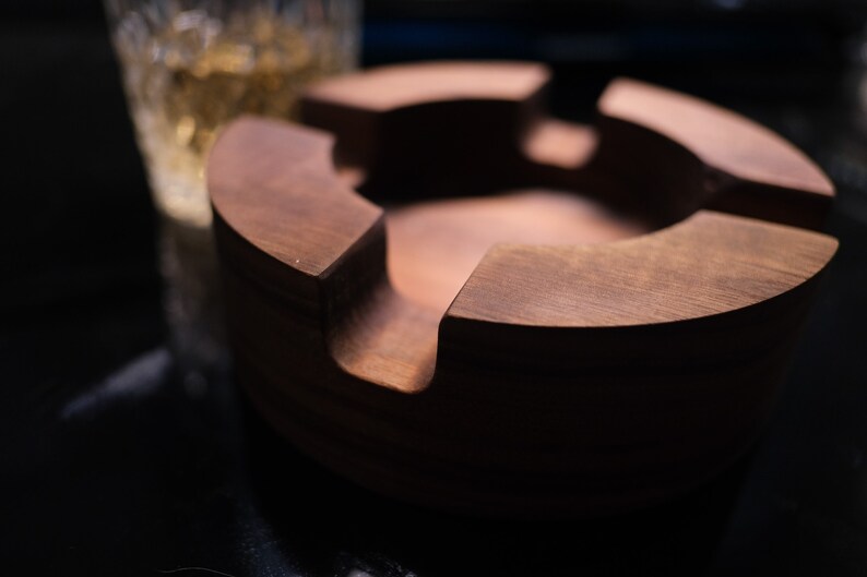 May include: A dark brown wooden ashtray with four compartments. The ashtray is round and has a smooth, polished finish.