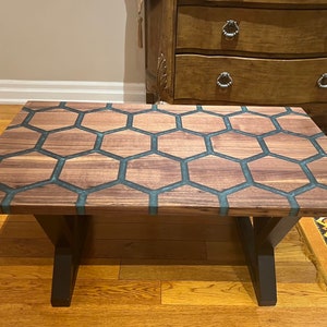 May include: A rectangular coffee table with a unique honeycomb design. The tabletop features a pattern of wooden hexagons filled with a teal-colored resin. The table has dark brown legs and a natural wood grain finish.