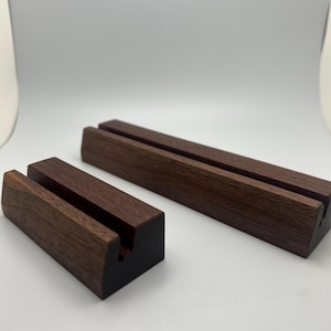 May include: Two wooden display stands. One is rectangular and long, the other is smaller and cube-shaped. Both are made of dark brown wood with a slot cut into the top for holding items. The stands are on a white background.