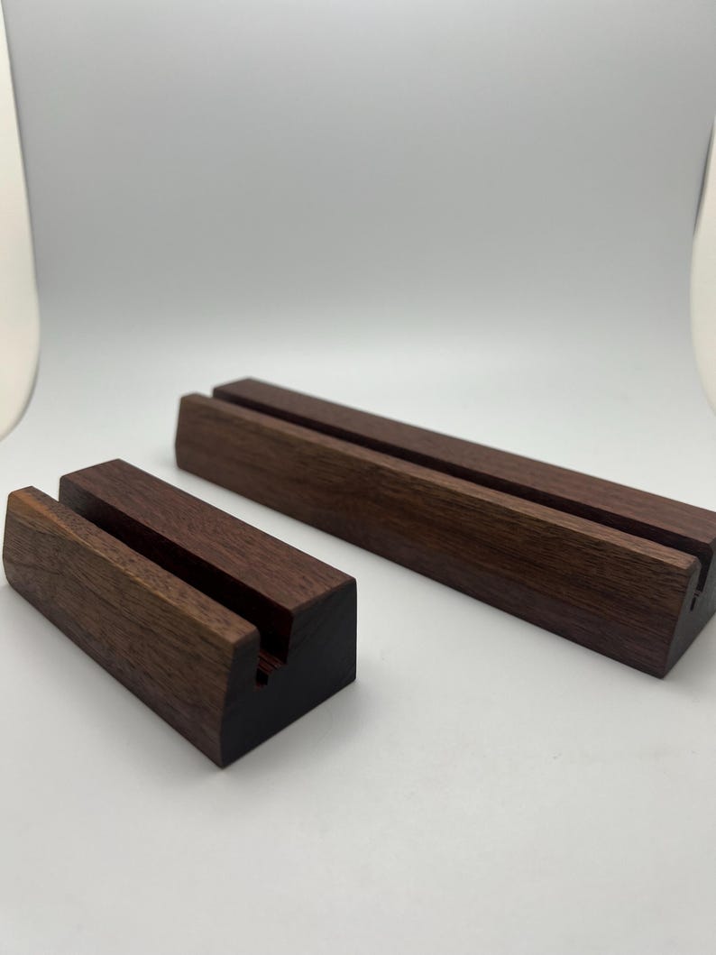 May include: Two wooden display stands. One is rectangular and long, the other is smaller and cube-shaped. Both are made of dark brown wood with a slot cut into the top for holding items. The stands are on a white background.