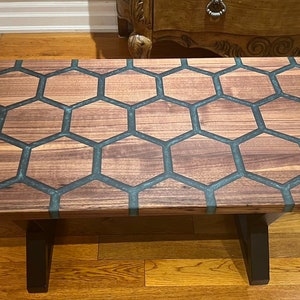 May include: A rectangular coffee table with a wooden honeycomb design. The table features a dark wood grain pattern with dark gray epoxy resin filling the hexagonal shapes. The table has black legs.