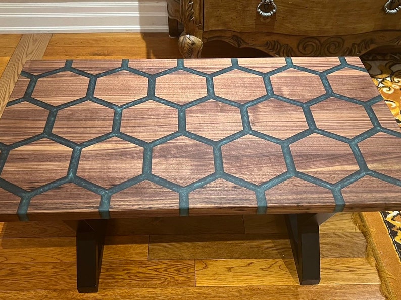 May include: A rectangular coffee table with a wooden honeycomb design. The table features a dark wood grain pattern with dark gray epoxy resin filling the hexagonal shapes. The table has black legs.