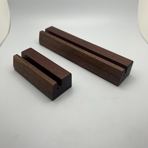 May include: Two wooden display stands. The stands are rectangular with a dark brown finish. Each stand has two parallel grooves cut into the top surface. The stands are designed to hold items upright. One stand is smaller than the other.
