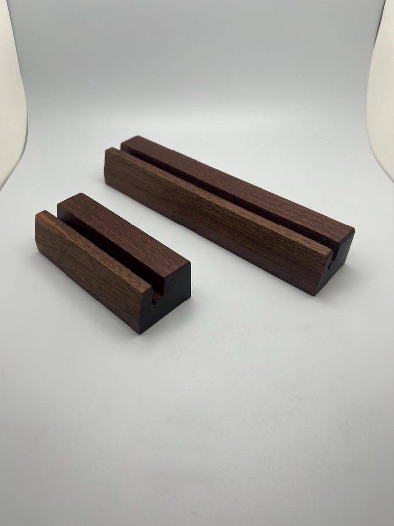 May include: Two wooden display stands. The stands are rectangular with a dark brown finish. Each stand has two parallel grooves cut into the top surface. The stands are designed to hold items upright. One stand is smaller than the other.
