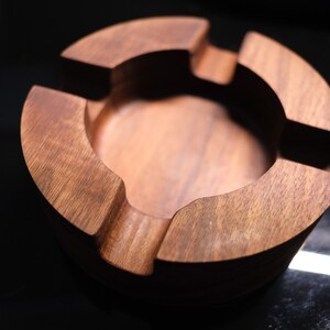 May include: A round wooden ashtray with four compartments. The ashtray is made of dark brown wood and has a smooth finish.