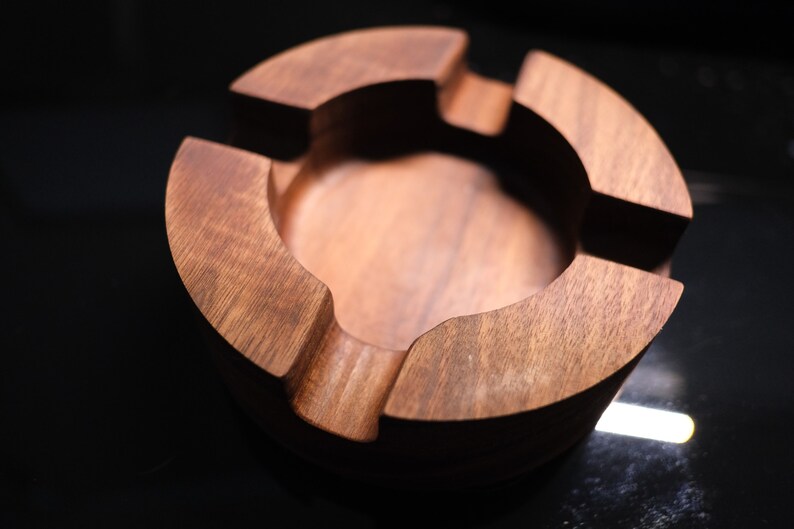 May include: A round wooden ashtray with four compartments. The ashtray is made of dark brown wood and has a smooth finish.