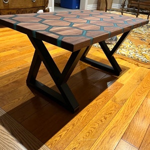 May include: A rectangular coffee table with a dark wood surface featuring a honeycomb design with teal resin inlays. The table has black metal X-shaped legs and sits on a hardwood floor.