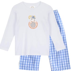 Può includere: Maglia da pigiama bianca a maniche lunghe e pantaloni da pigiama a quadri blu. La maglia presenta un montone ricamato con un berretto da baseball e le iniziali "RBB" all'interno di un pallone da basket. Il pigiama è progettato per il comfort e lo stile.