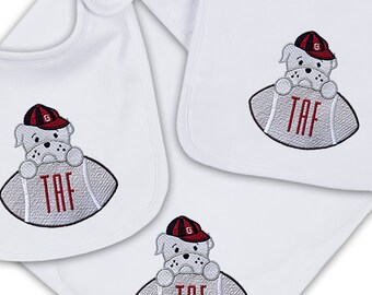 May include: White baby bibs and a receiving blanket with an embroidered bulldog design. The bulldog is wearing a red and black cap and holding a football with the letters "TAF". The bibs have a snap closure.