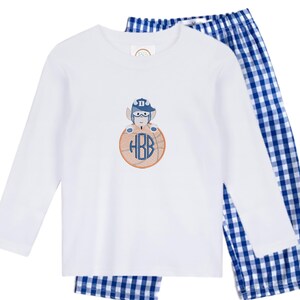 May include: White long-sleeved pajama top with an embroidered design of a baseball player on a baseball. The baseball has the initials HBB in a blue font. The pajama pants are blue and white checkered.