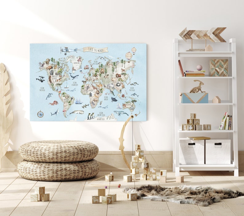 May include: A light blue world map with illustrations of animals and plants from different continents. The map is printed on canvas and has the text "Carte du Monde" at the top. The map is hanging on a white wall in a room with a wooden floor and a white bookshelf with wooden shelves.