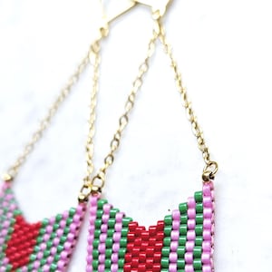 Op de afbeelding: Handgemaakte kralen oorbellen met een chevron ontwerp. De oorbellen hebben een gouden ketting en sluiting, en het kralenpatroon bevat rode, groene en roze kralen. Een uniek accessoire.