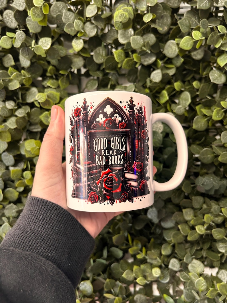 May include: White ceramic mug with a gothic-style design featuring a black archway with red roses and the text "GOOD GIRLS READ BAD BOOKS".
