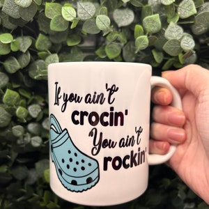 May include: White ceramic mug with a blue and black illustration of a Croc shoe and the text "If you ain't crocin' you ain't rockin'"