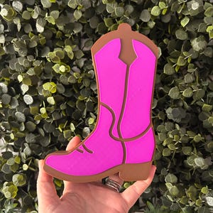 May include: A pink cowboy boot cutout with a brown outline. The boot is made of a thick, durable material and is ideal for crafting projects.