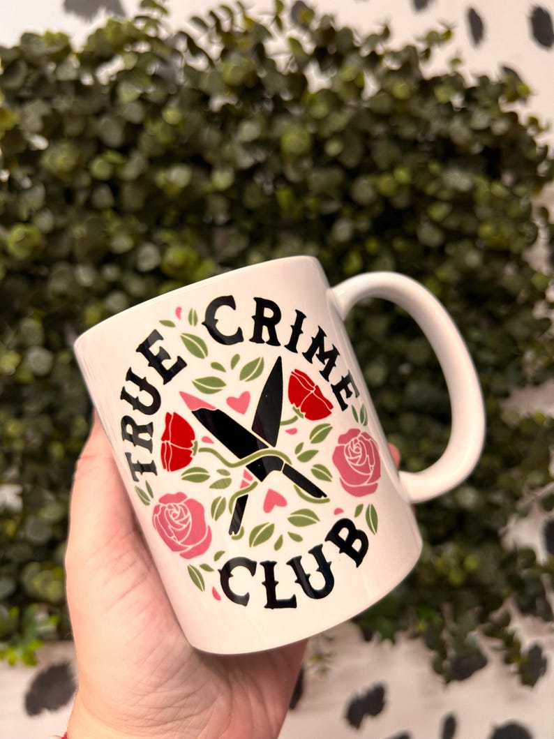 May include: White ceramic mug with a black design that says "True Crime Club" with a pair of crossed knives and roses in pink and red.
