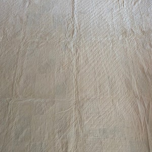 Op de afbeelding: Een close-up van een witte gestikte stof met een ruitpatroon. De stof is gekreukt en heeft een licht getextureerd oppervlak.