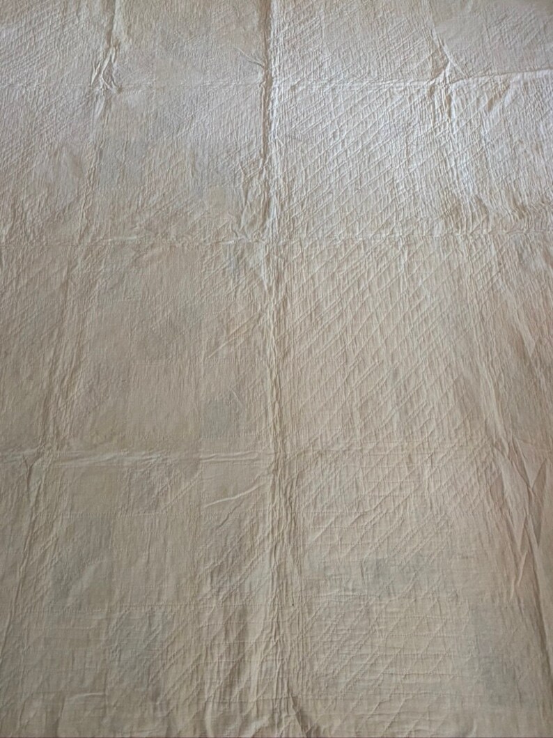 Op de afbeelding: Een close-up van een witte gestikte stof met een ruitpatroon. De stof is gekreukt en heeft een licht getextureerd oppervlak.