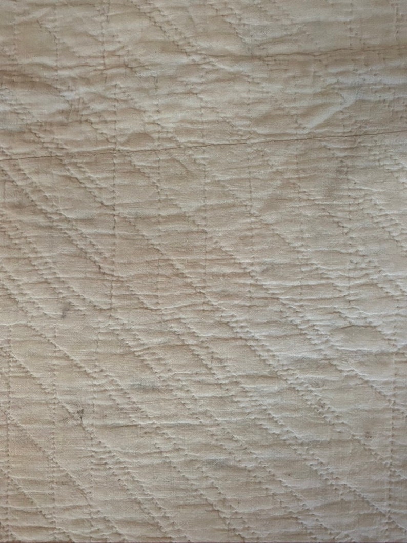 Op de afbeelding: Een close-up van een witte gestikte stof met een ruitpatroon. De stof is textuurrijk en heeft een subtiele glans.