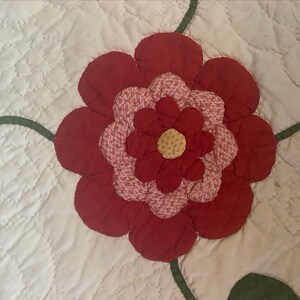 Op de afbeelding: Een rode en roze bloem met een gele kern, gequilt op een witte achtergrond.