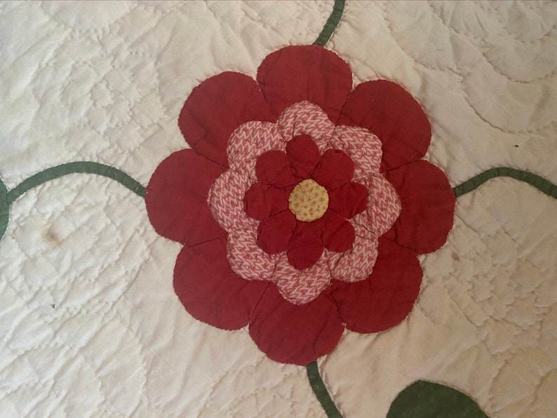 Op de afbeelding: Een rode en roze bloem met een gele kern, gequilt op een witte achtergrond.