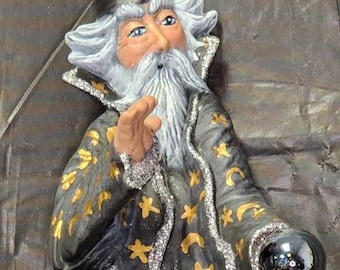 Op de afbeelding: Een fantasievol tovenaarsbeeldje met een lange, vloeiende robe versierd met gouden sterren en halve manen. Hij draagt een puntige hoed en houdt een zwarte kristallen bol in zijn hand.