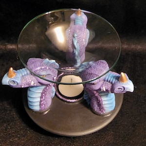 May include: A purple and blue dragon-shaped oil burner with three heads and a glass dish on top. The burner is made of ceramic and has a gold accent on each head.