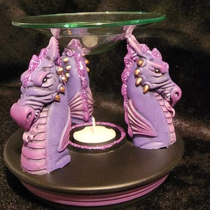 May include: Purple dragon-shaped ceramic oil burner with a glass dish and a tealight candle holder. The burner has a black base with a purple stripe.