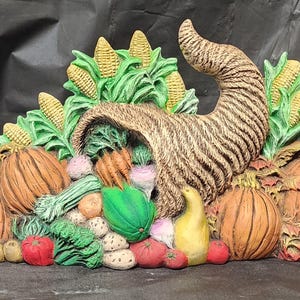 May include: A decorative cornucopia overflowing with autumn harvest items. The centerpiece features a woven horn filled with vegetables, surrounded by pumpkins, corn, and other produce in shades of orange, green, and yellow. A festive autumn decoration.