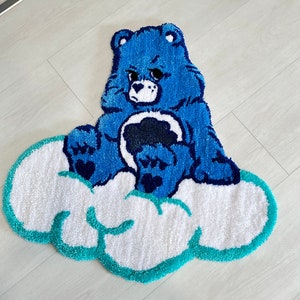 May include: Blue Care Bear rug with a grumpy expression sitting on a white cloud with a turquoise outline.
