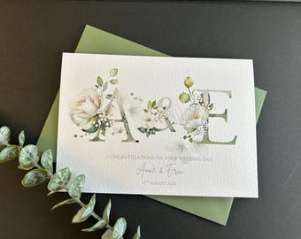 May include: A wedding card with the initials "A & E" is decorated with floral arrangements. The card is on a green envelope, with the words "Congratulations on your wedding day" and the names "Anne & Eric" and the date "17th August 2025".