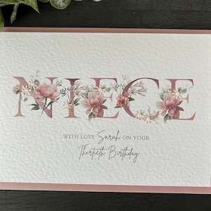 K&ouml;nnte beinhalten: Eine wei&szlig;e Karte mit rosa Rand. Das Wort "NIECE" ist in gro&szlig;en Buchstaben mit rosa Blumen und Gr&uuml;n um jeden Buchstaben geschrieben. Der Text "With love Sarah on your Thirtieth Birthday" steht unter dem Wort "NIECE".