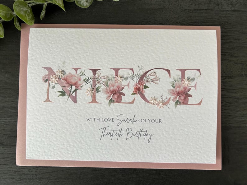 K&ouml;nnte beinhalten: Eine wei&szlig;e Karte mit rosa Rand. Das Wort "NIECE" ist in gro&szlig;en Buchstaben mit rosa Blumen und Gr&uuml;n um jeden Buchstaben geschrieben. Der Text "With love Sarah on your Thirtieth Birthday" steht unter dem Wort "NIECE".