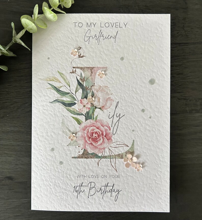 May include: A white card with a floral design and the text "To my lovely Girlfriend with love on your 16th Birthday".