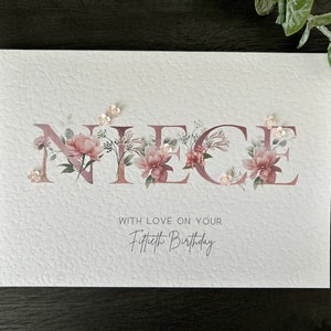 K&ouml;nnte beinhalten: Eine wei&szlig;e Karte mit dem Wort "NIECE" in pinken Blumenbuchstaben. Die Karte tr&auml;gt den Text "With love on your Fiftieth Birthday" unter den Blumenbuchstaben.