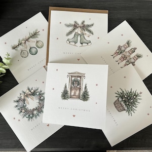 May include: A selection of Christmas cards featuring watercolour illustrations. Designs include ice skates, baubles, a wreath, a door, and a basket of greenery. Each card has the words "MERRY CHRISTMAS" printed on it.