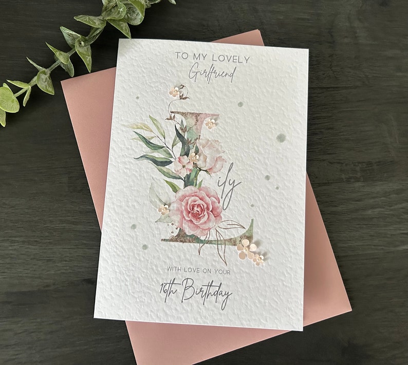 May include: A white card with a pink floral design and the text "To my lovely Girlfriend" and "With love on your 18th Birthday".