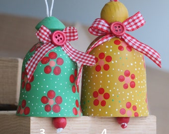 May include: Two wooden Christmas bells with red and white gingham ribbon bows. The bell on the left is green with red polka dots and the bell on the right is yellow with red polka dots.